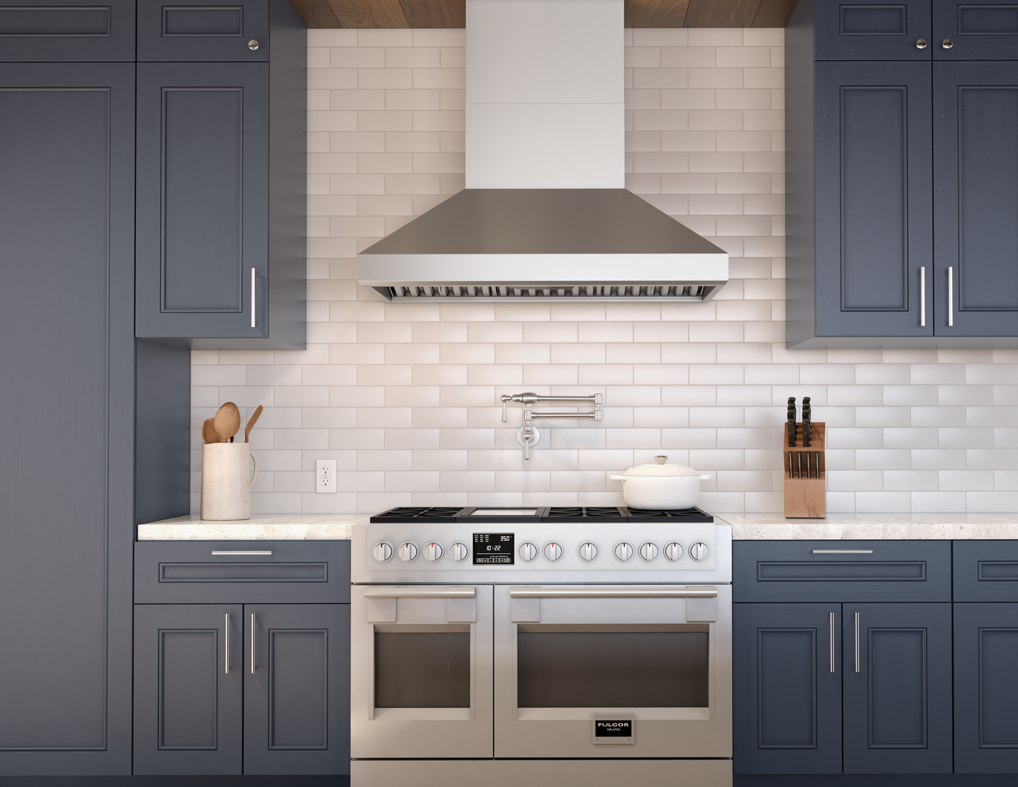 stainless steel chimney hood above double oven range in kitchen with blue cabinetry and white subway tile backsplash