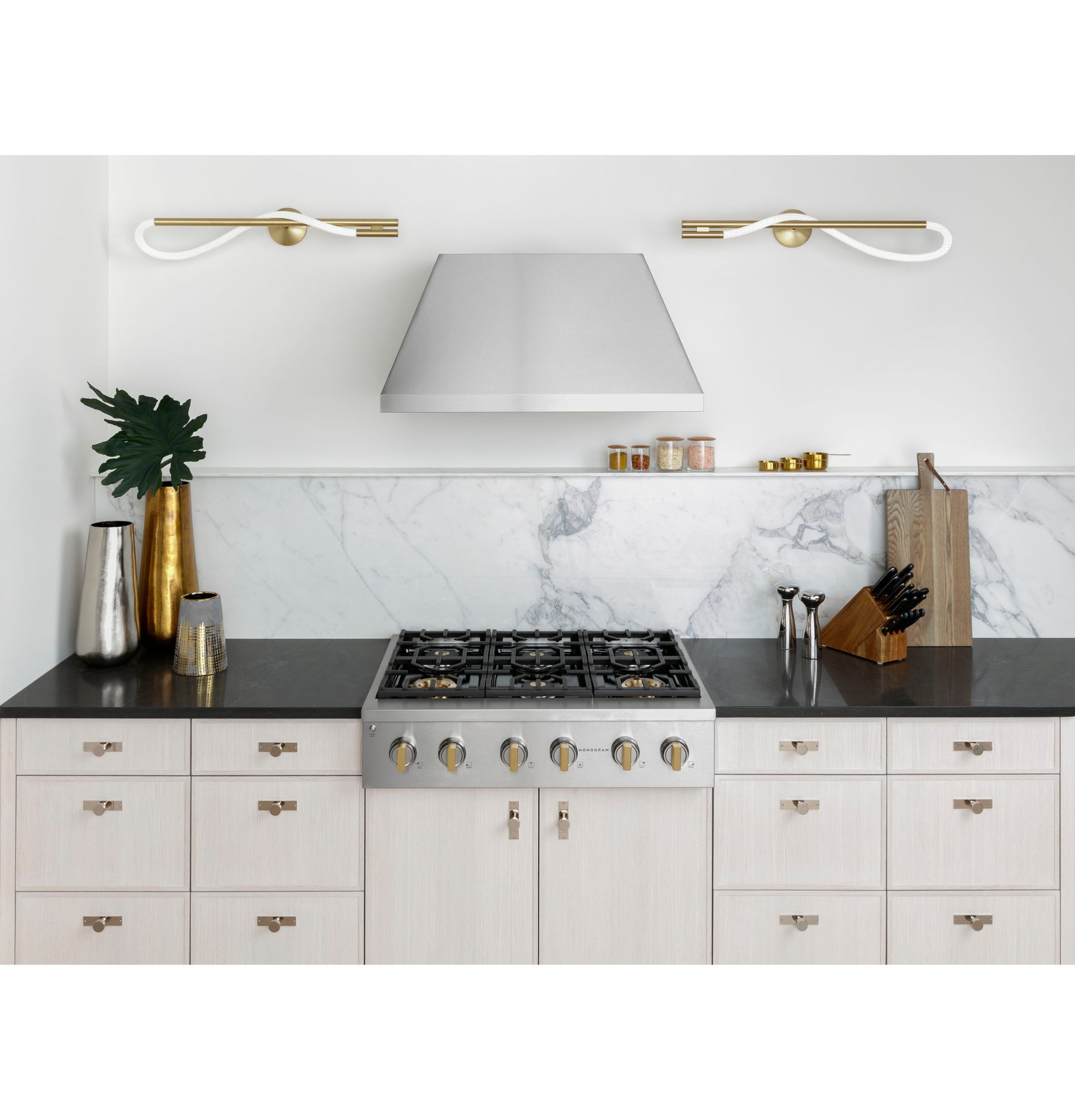 Stainless steel 36-inch gas rangetop with six burners installed in white kitchen cabinetry under modern range hood