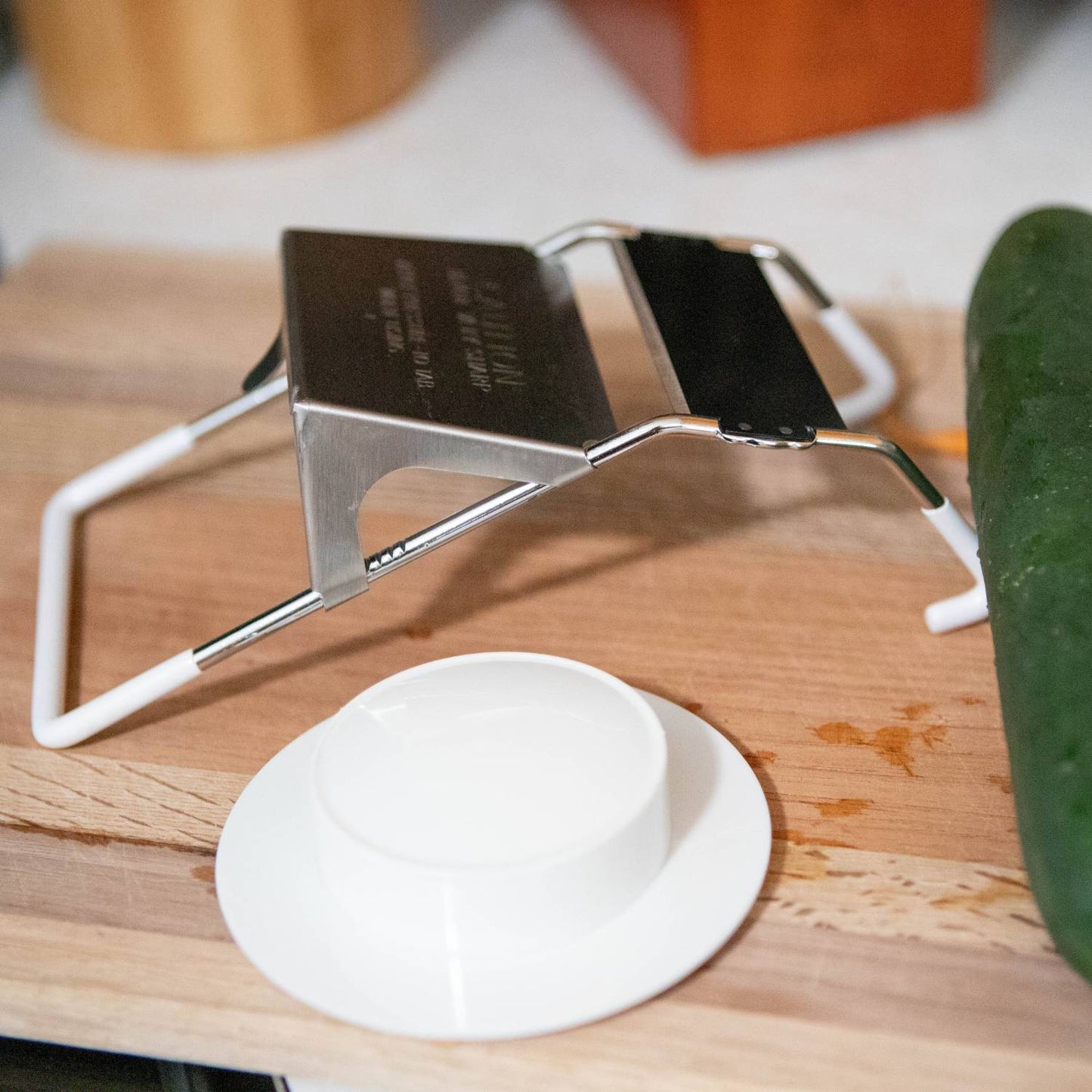 Mandoline slicer with stainless steel blade and white plastic hand guard on wooden cutting board in kitchenware collection