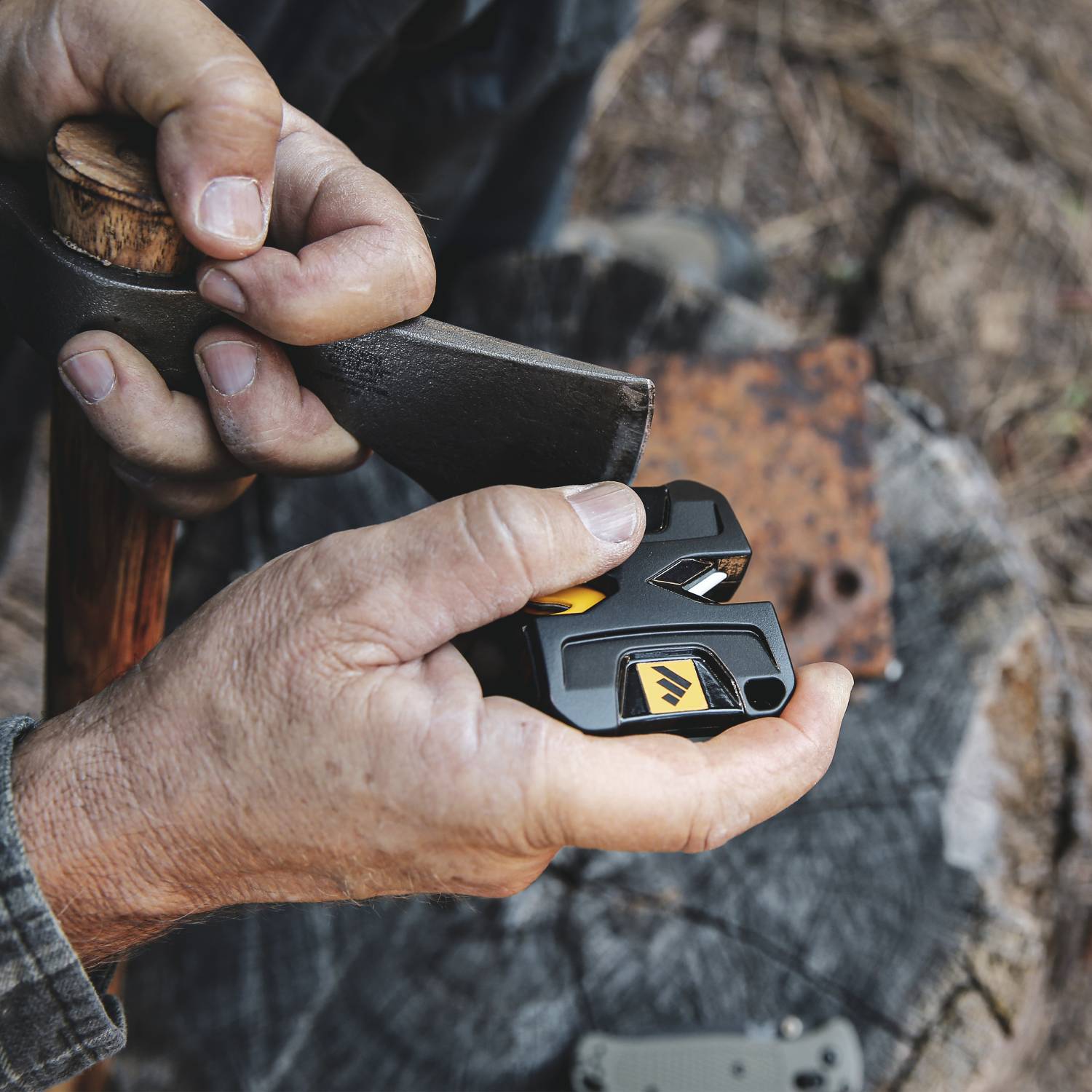 Person using compact black and yellow pivot sharpener to sharpen an axe blade for outdoor tools maintenance