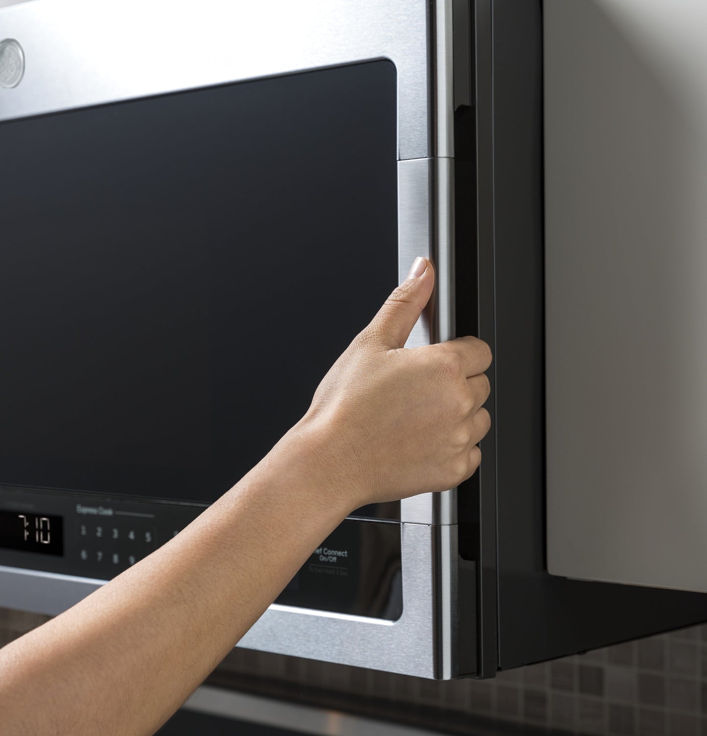 Hand opening stainless steel over-the-range sensor microwave door in modern kitchen appliances collection