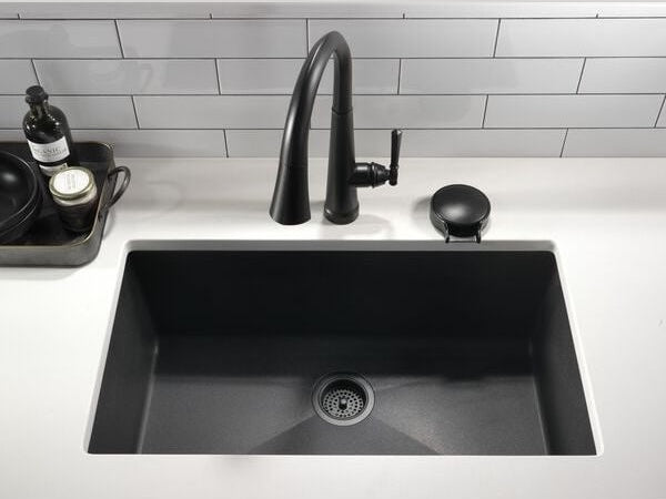 Matte black single handle pull-down kitchen faucet installed with deep black rectangular sink in white countertop setting