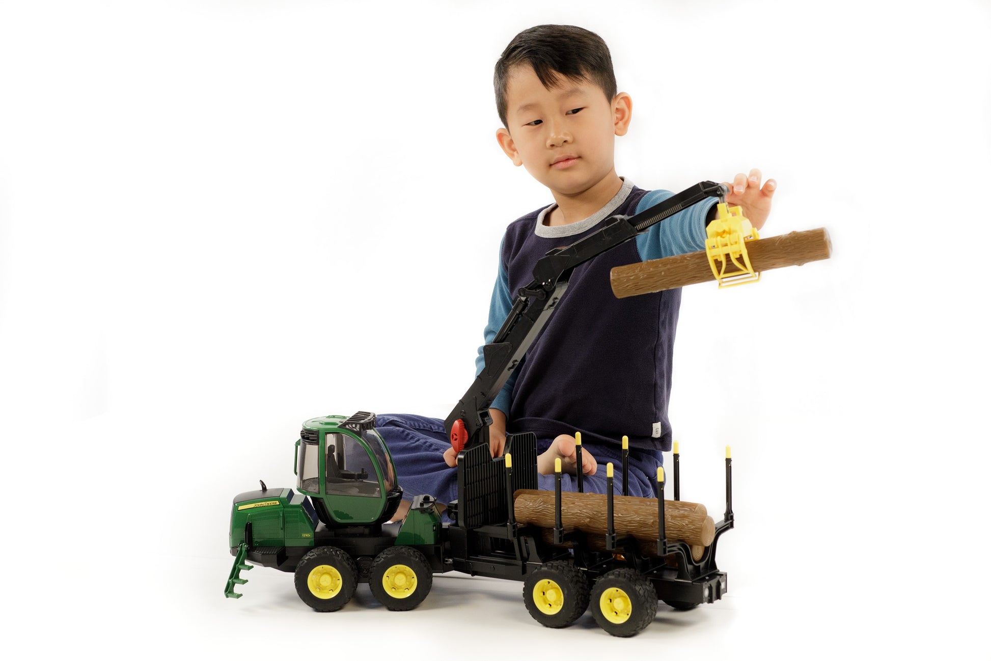 Child operating Bruder John Deere 1210E Forwarder toy with crane lifting wooden log for tools and home improvement play