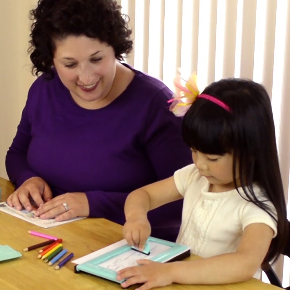 Young girl and woman engaged in creative pretend play drawing with colored pencils at wooden table indoors