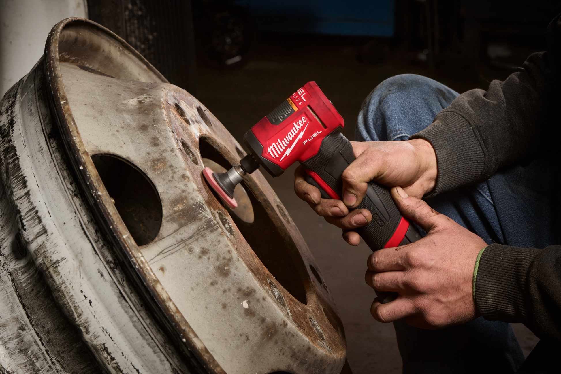 Handheld red and black cordless right angle die grinder polishing a rusted metal wheel in a workshop setting