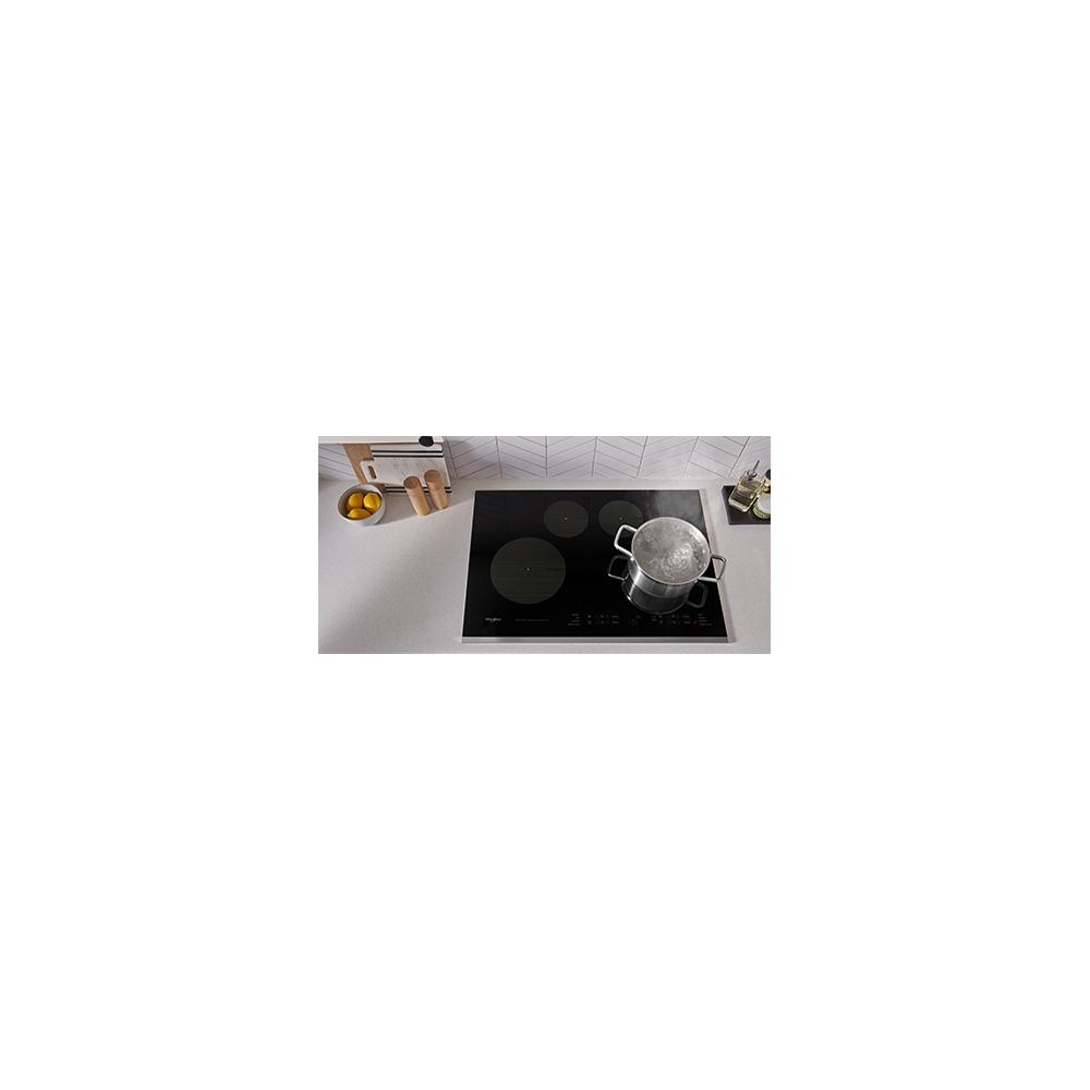 Black glass induction cooktop with pot boiling water, set in white countertop with kitchen accessories nearby
