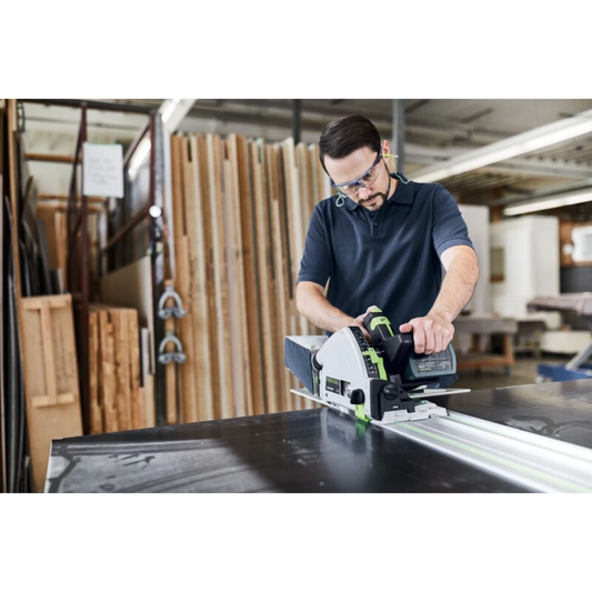 Man using a power saw on a Festool guide rail for precise cuts in a woodworking shop setting with safety glasses