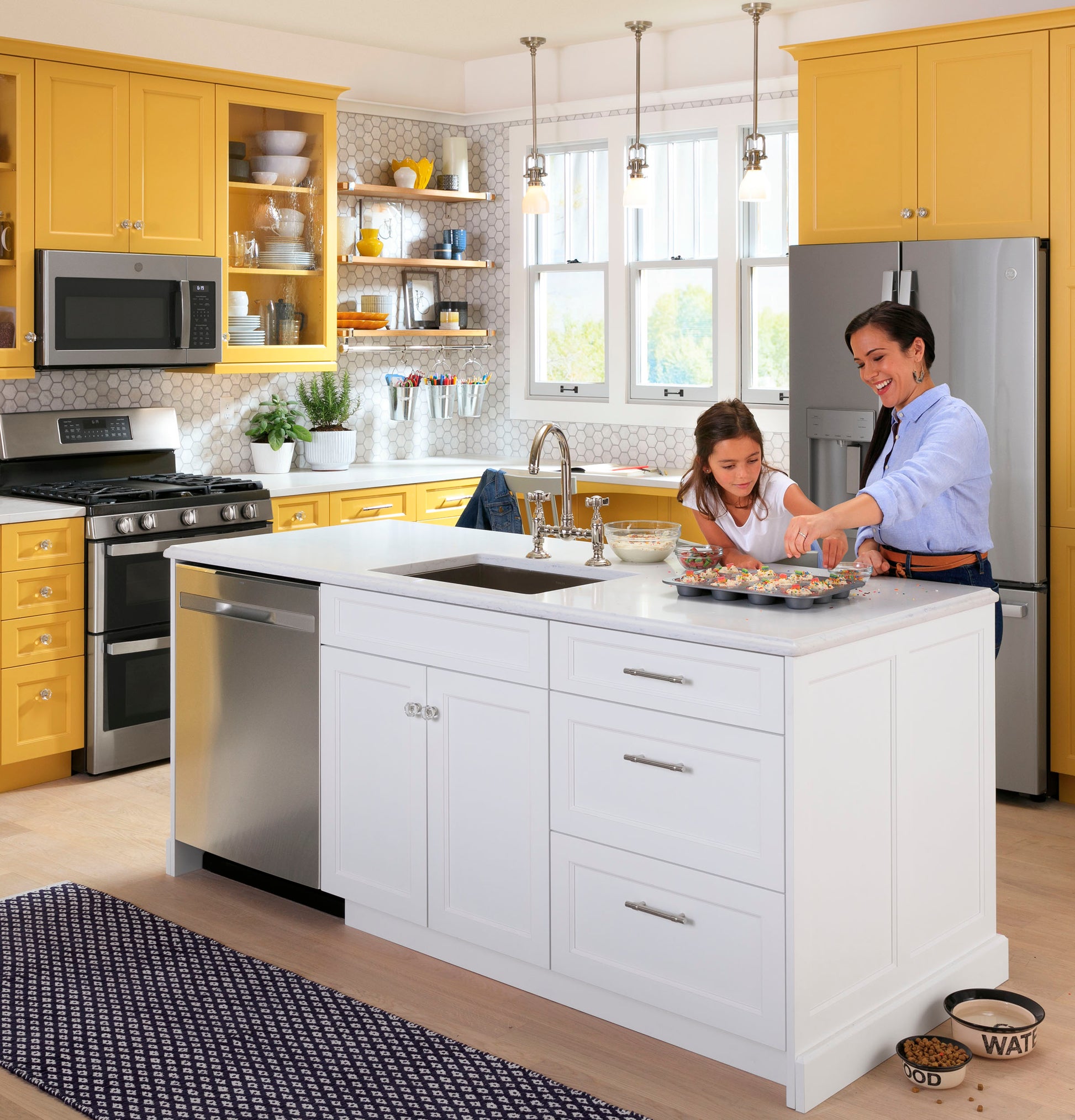 Modern kitchen with yellow cabinets and white island featuring stainless steel dishwasher and gas double oven range from Ranges collection