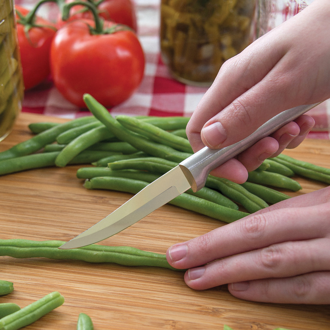 Hand holding sharp paring knife with smooth satin finish handle slicing green beans on wooden board in Kitchenware collections