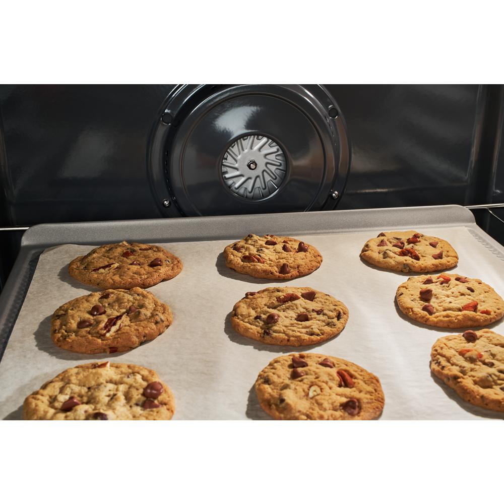 Chocolate chip cookies baking on parchment paper inside an oven with a visible circular convection fan element