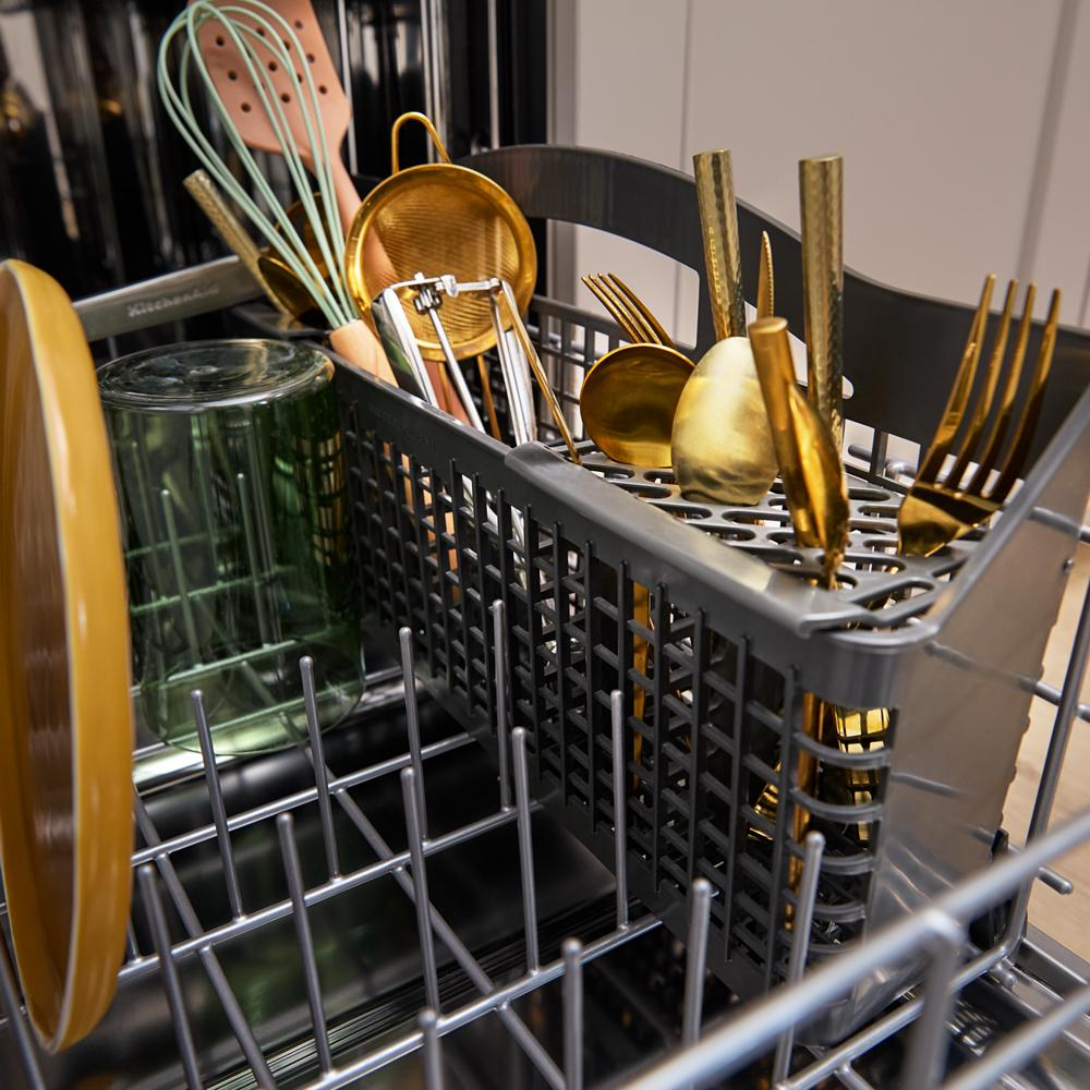Third level utensil rack inside dishwasher loaded with gold flatware, kitchen tools, and glassware in modern appliance setting