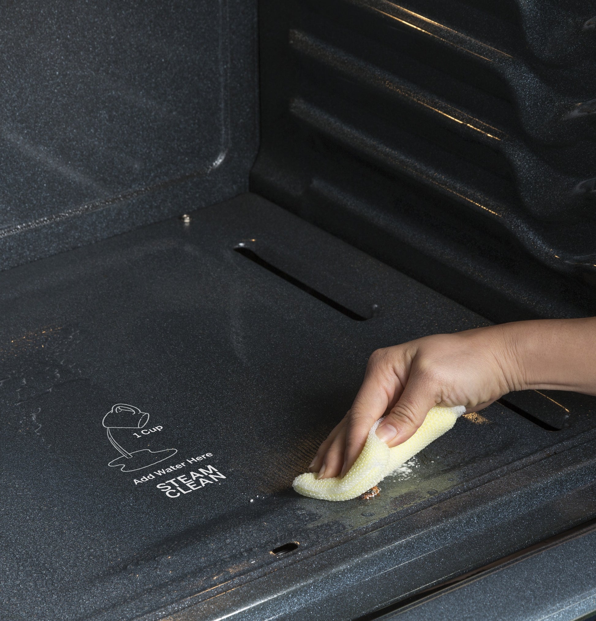 Hand cleaning the inside of a dark oven cavity using a yellow cloth for home improvement appliances.