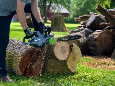 Person cutting thick log outdoors using EGO Power+ cordless 18-inch chainsaw for home improvement tasks