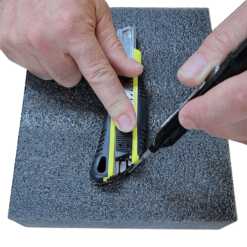 Hands cutting black dense foam with utility knife for woodworking tool storage and workshop organization use