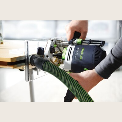 Person operating a Festool router with dust extraction on a light wood panel for precise home improvement tasks