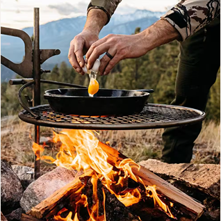 Round metal grill grate with adjustable anchor arm set over wood fire pit in outdoor living and patio furniture setting
