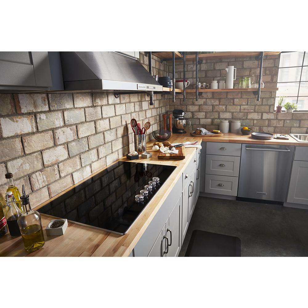 Sleek black electric cooktop with five radiant elements and knob controls installed in modern kitchen with brick backsplash