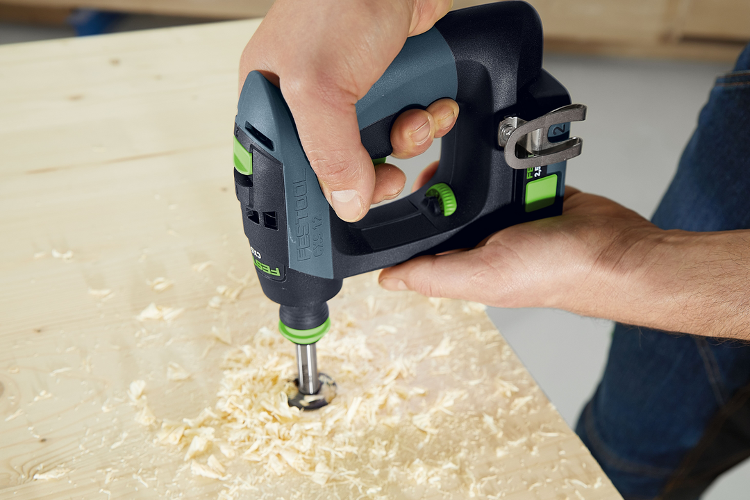 Person using compact cordless drill to bore a hole in light wood with wood shavings in workshop setting