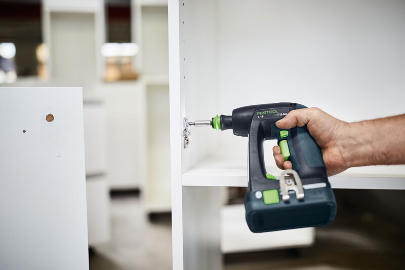 Hand holding Festool cordless drill fastening screws on white furniture during home improvement task