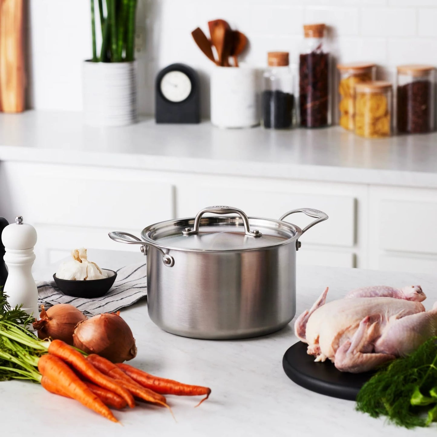 Stainless steel 5-quart fully clad sauce pot with lid on kitchen counter, surrounded by vegetables and raw poultry