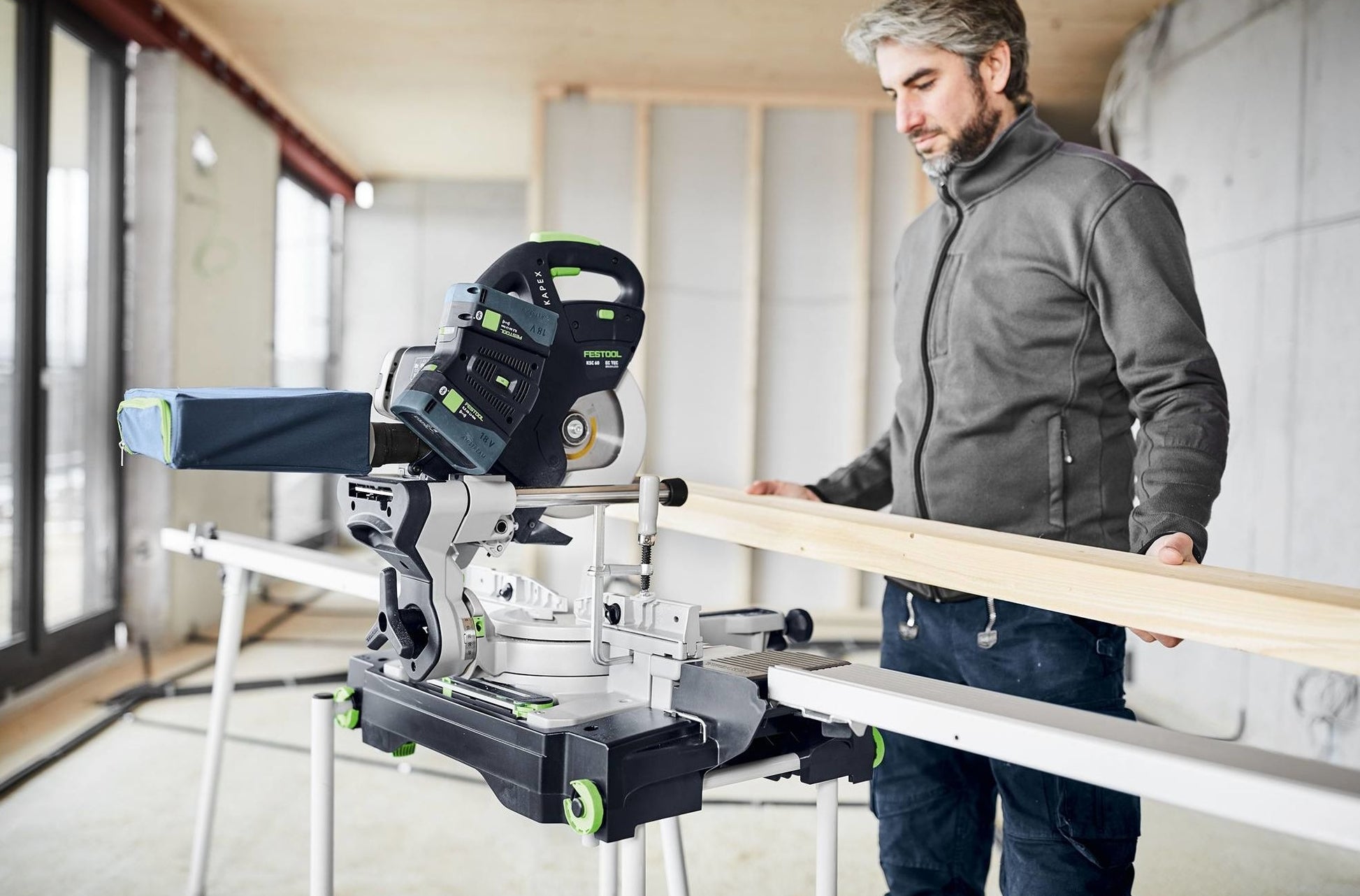 Man using cordless sliding compound miter saw on wood plank in unfinished room with natural light for home improvement