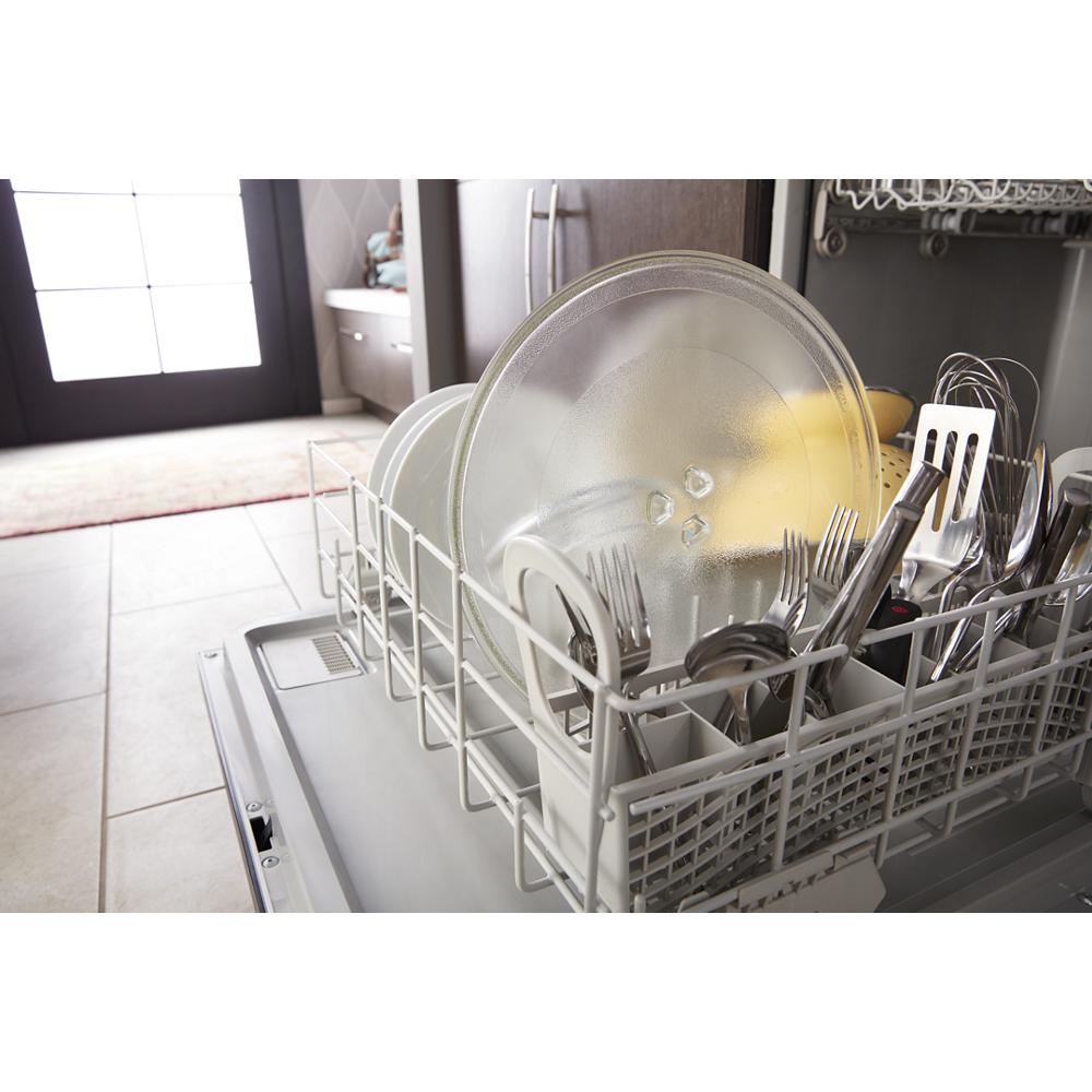 Open dishwasher loaded with plates, glass lids, utensils, and kitchen tools in a bright kitchen setting