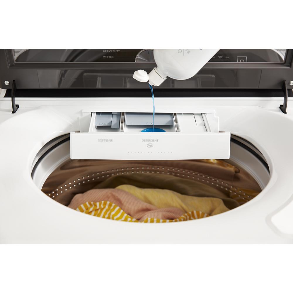 Top-loading washing machine with detergent dispenser being filled and colorful clothes inside drum