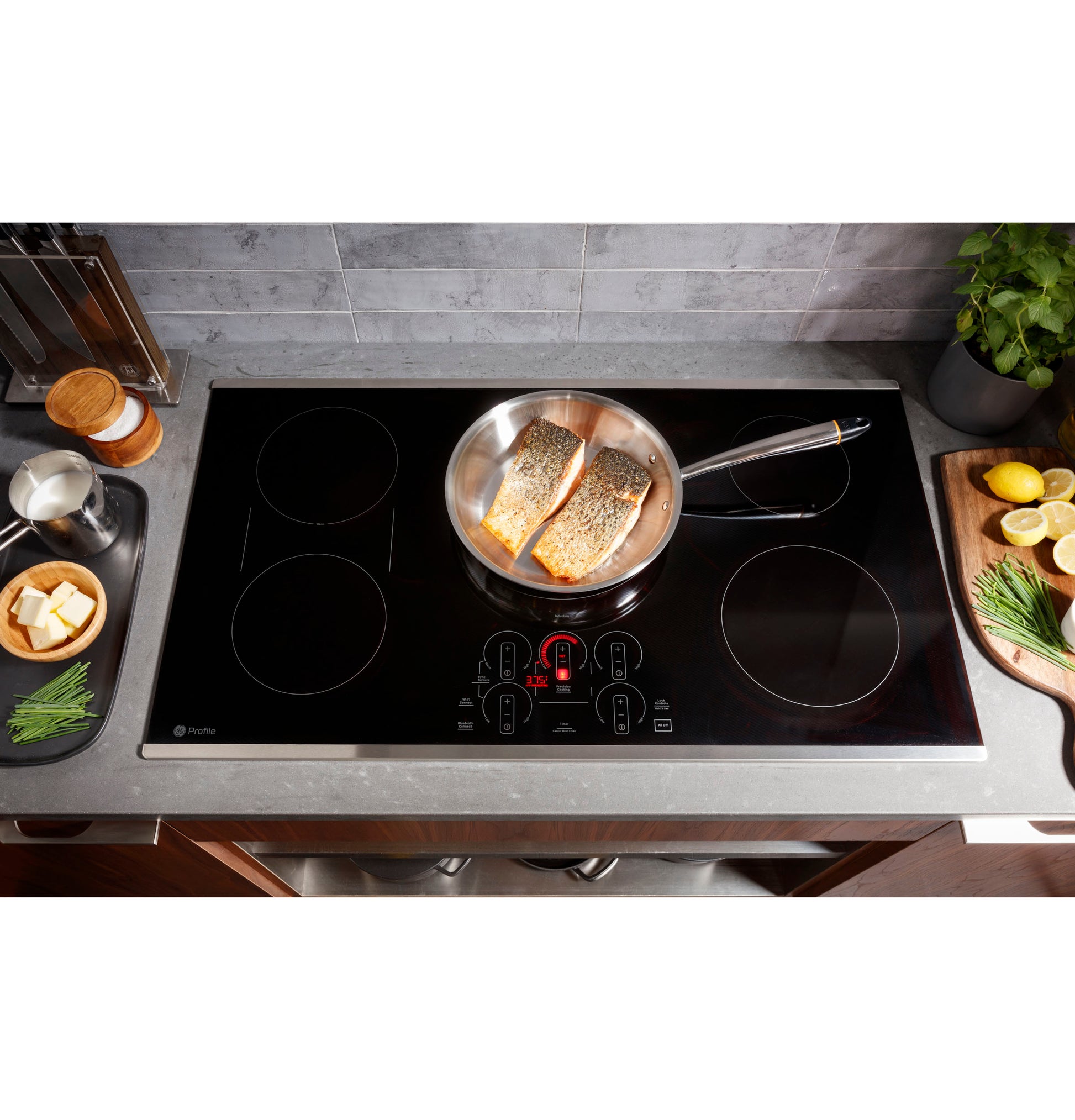 Modern black glass induction cooktop with touch controls cooking salmon in stainless steel pan on kitchen countertop