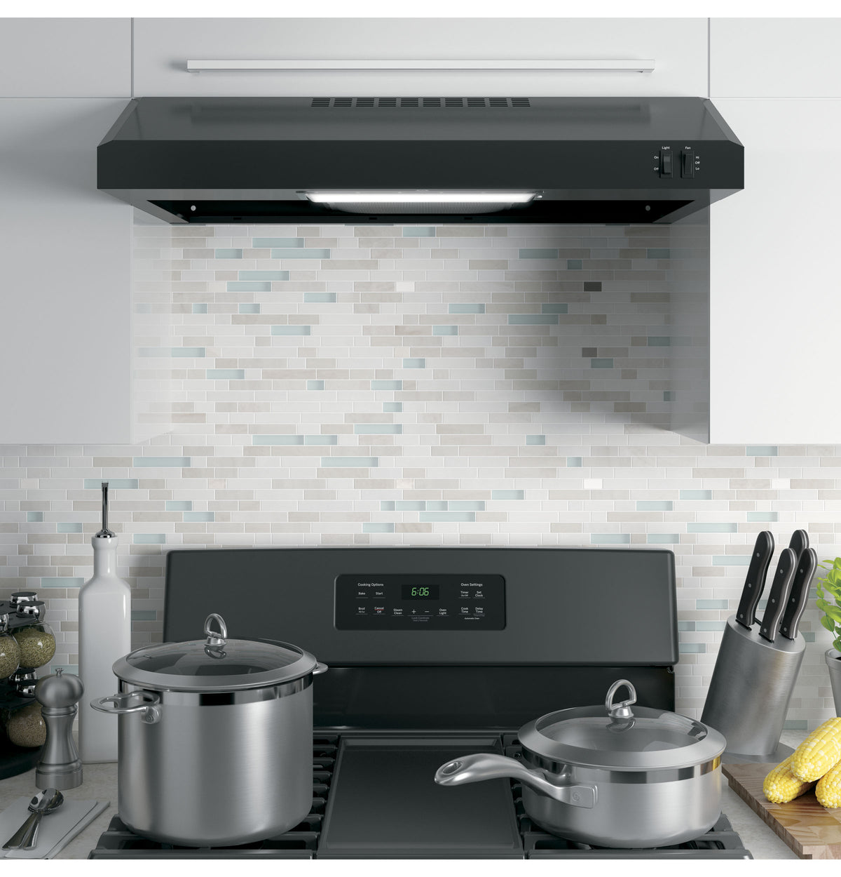 Black under cabinet range hood with light installed above stovetop in modern kitchen with cooking pots and knives