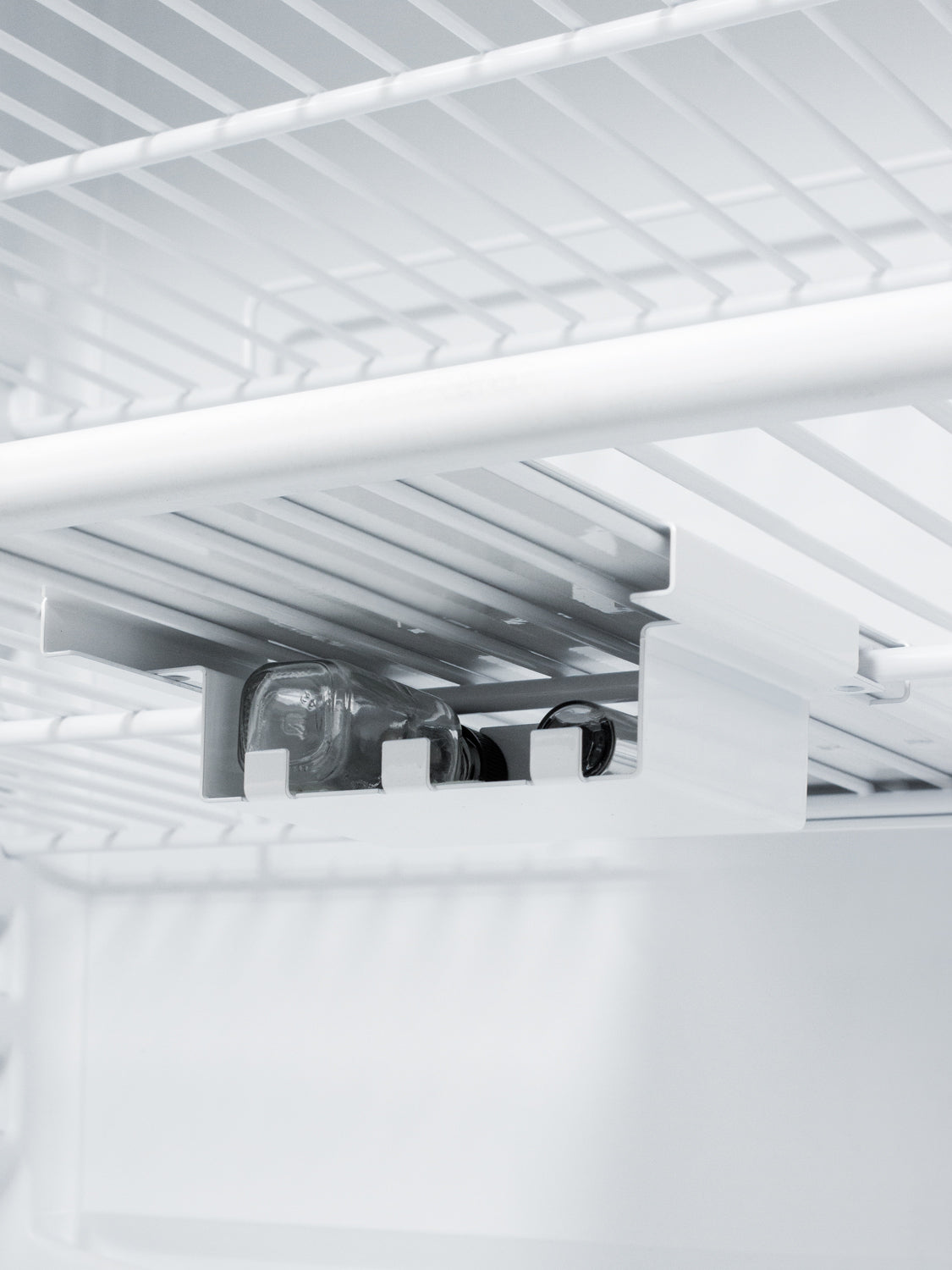 White refrigerator interior with wire shelving and specialized storage rack holding glass bottles for kitchen appliances use