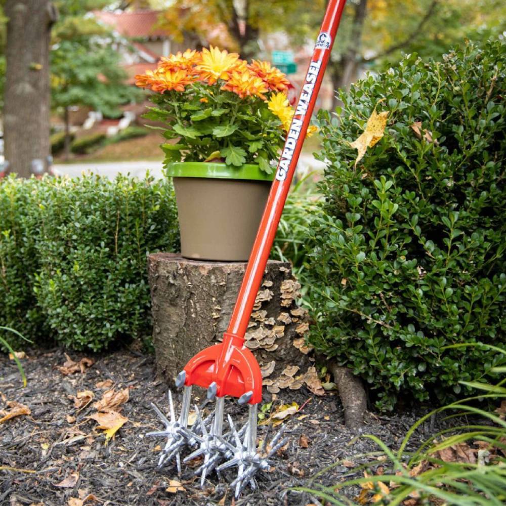 Steel garden cultivator with red handle and star-shaped rotating tines breaking soil in outdoor gardening tools collection