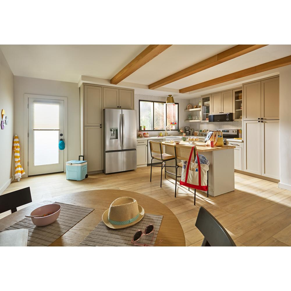Bright kitchen with beige cabinetry, stainless steel fridge, wooden floor, and dining table with summer accessories.