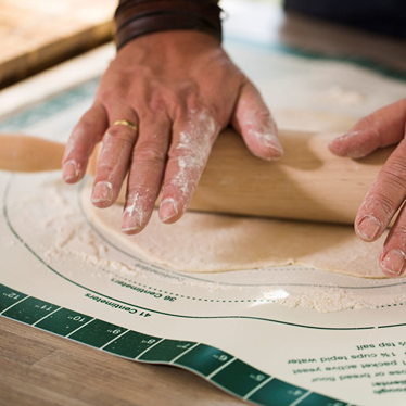 Hands rolling dough on a measuring and instruction dough mat for outdoor grilling and cooking accessories collections