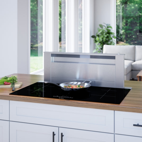 Black induction cooktop with five cooking zones and integrated downdraft vent cooking vegetables in kitchen setting