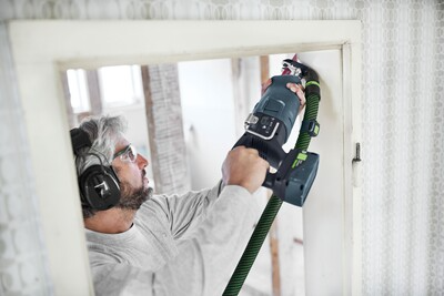 Man wearing hearing protection using Festool dust extraction adapter with power tool for home improvement task