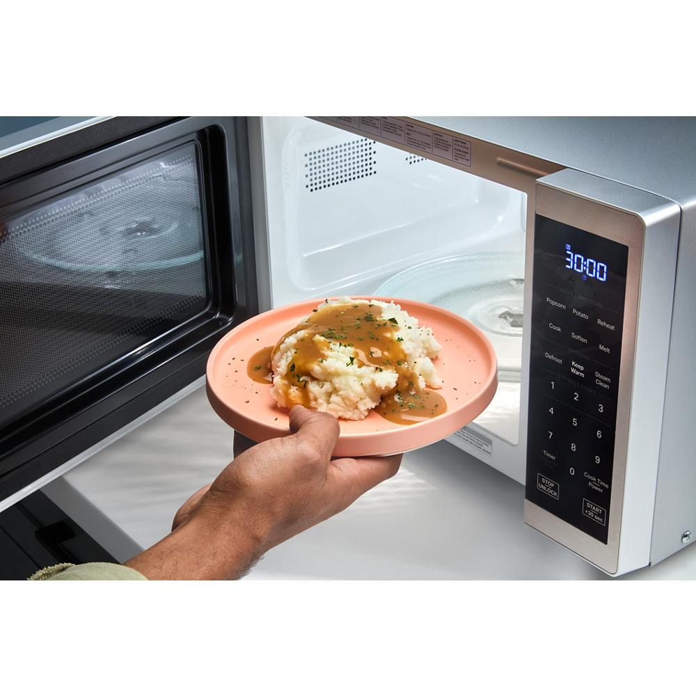 Hand removing plate of mashed potatoes with gravy from open microwave interior showing digital control panel and LED display