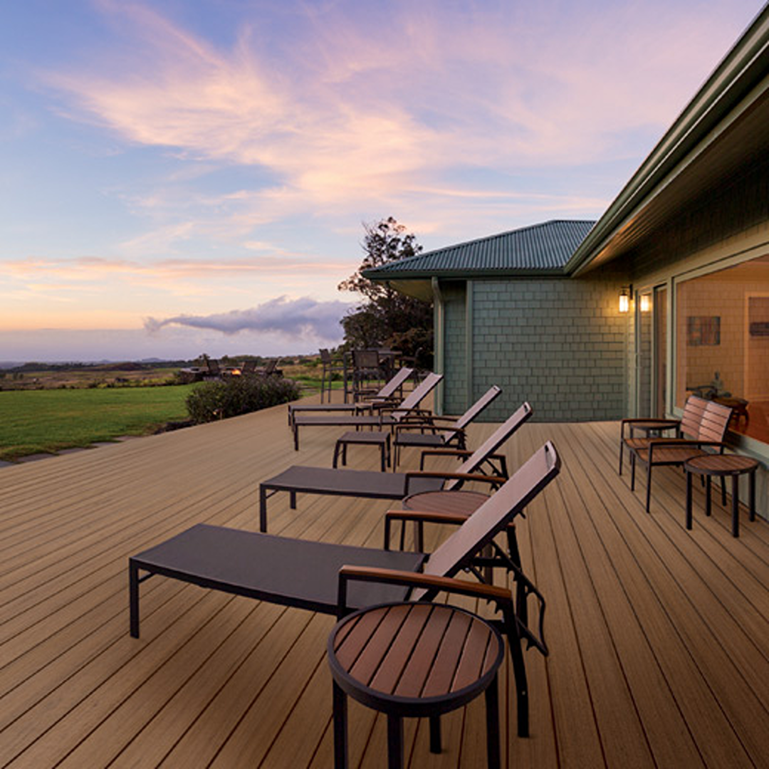 Outdoor deck with coconut husk finish fascia board featuring lounge chairs and small tables at sunset