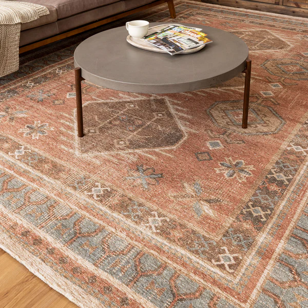 Traditional muted red and blue antique-inspired rug with floral and geometric patterns under a round modern coffee table