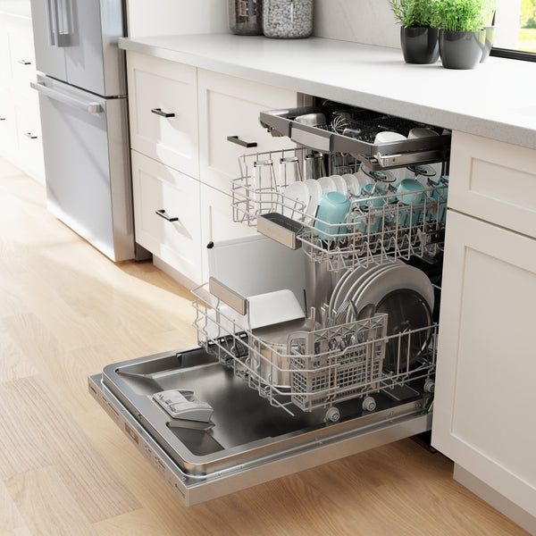 Open stainless steel dishwasher with clean white plates, bowls, and light blue mugs inside under white kitchen countertop