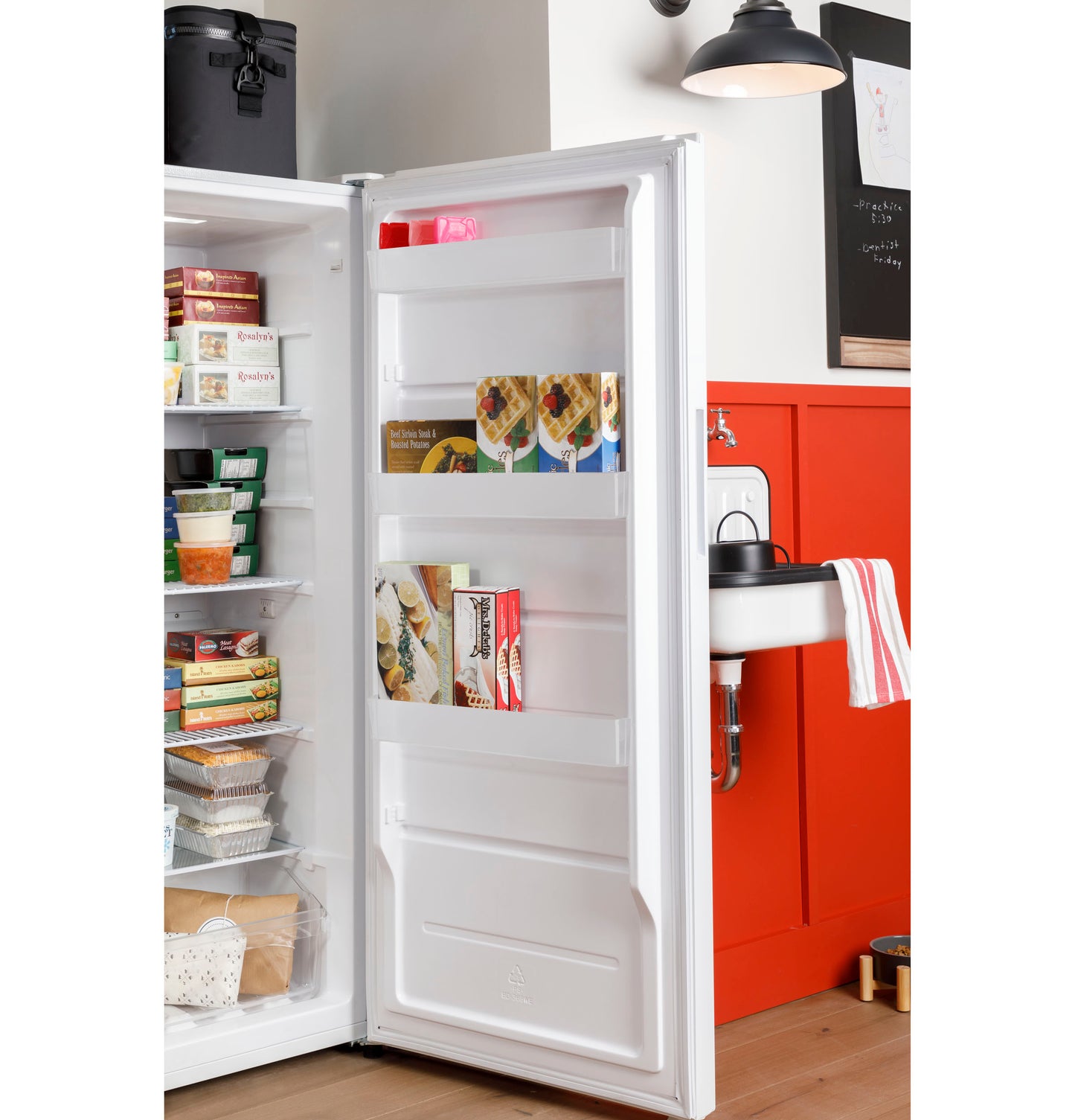 Open white upright freezer door showing organized frozen food inside in modern kitchen and laundry area