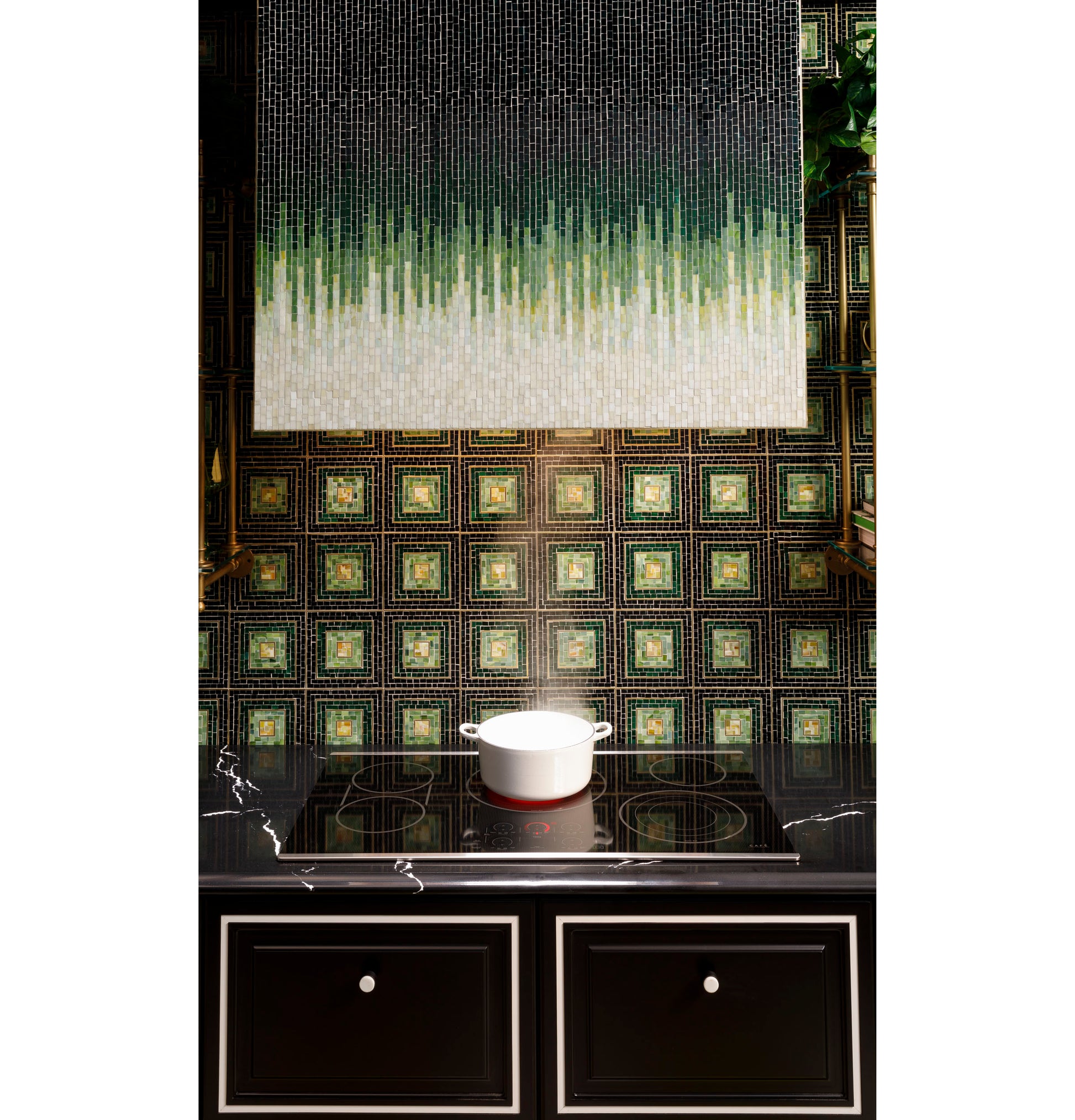 White pot simmering on black glass touch-control electric cooktop with decorative green and gold tiled backsplash