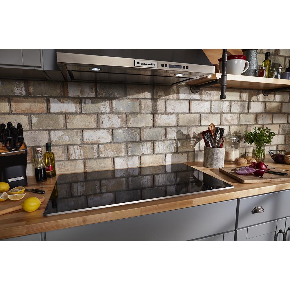 Black glass electric cooktop with five touch-activated elements in kitchen featuring brick backsplash and wood counters