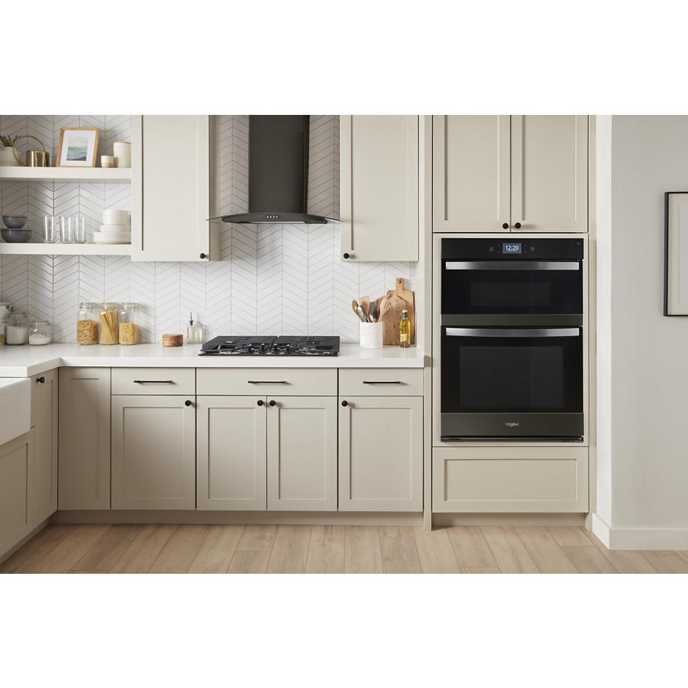 Modern kitchen with light cabinetry, stainless steel gas cooktop, built-in double oven, and black wall-mounted range hood
