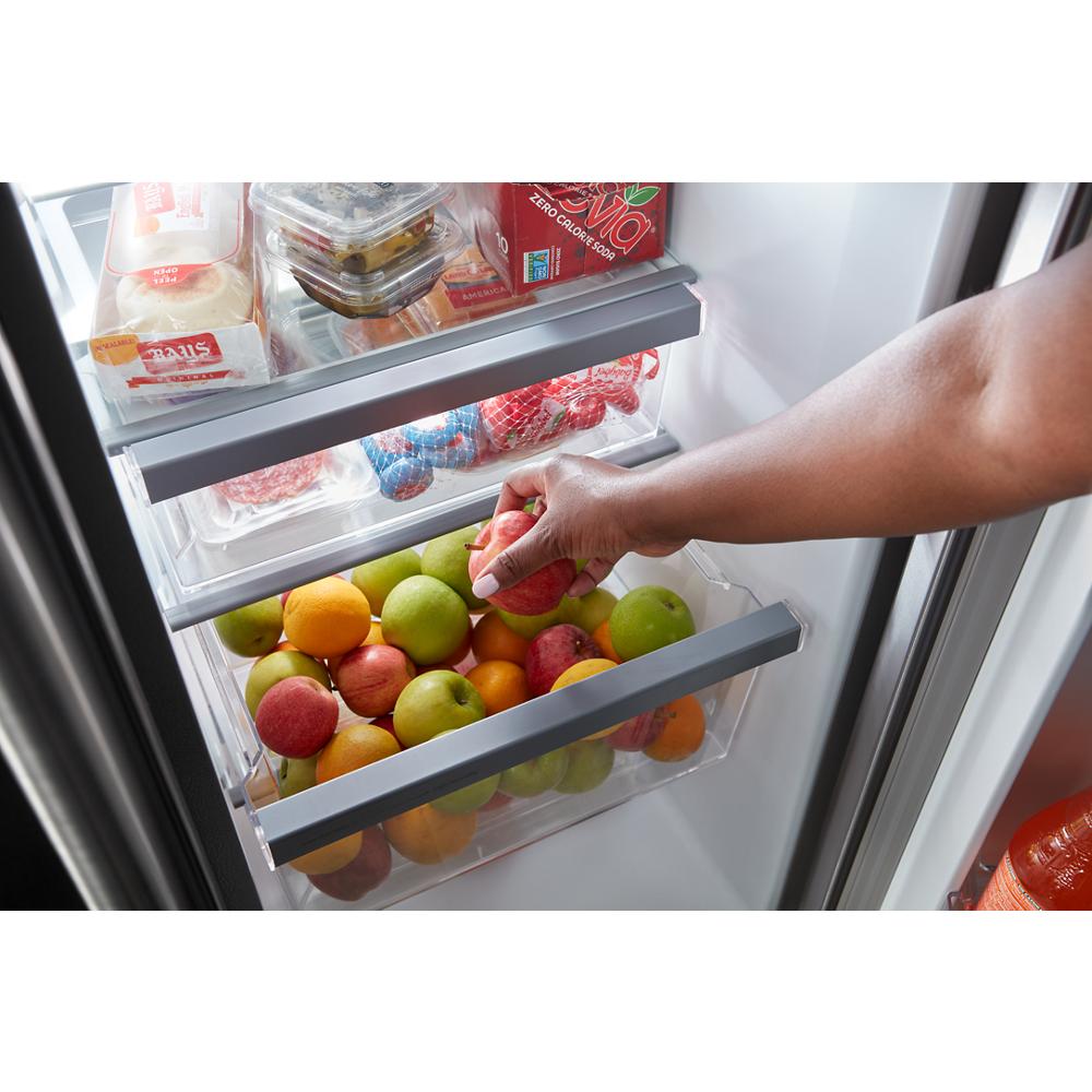 Hand reaching into fresh fruit drawer filled with apples and oranges inside a side-by-side refrigerator door in Appliances collection