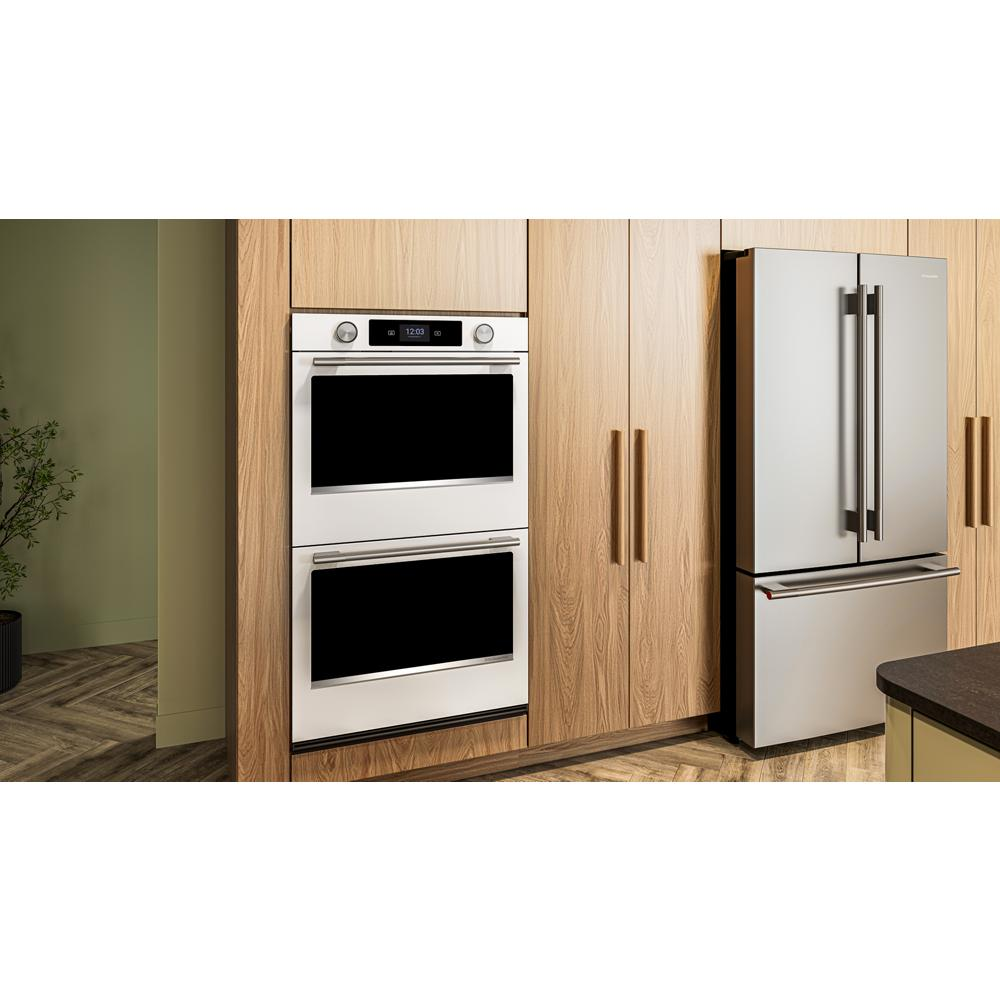 Double wall oven in white with LED display and stainless handles installed in natural wood kitchen cabinetry next to stainless steel fridge