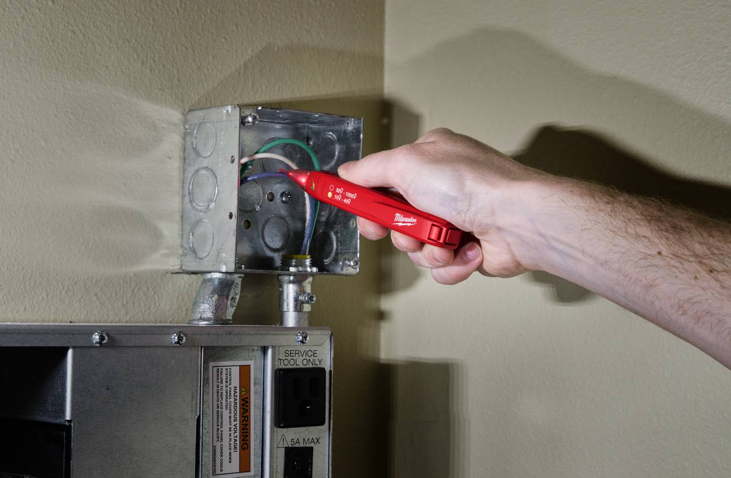 Hand using a red Milwaukee dual range voltage detector to test electrical wiring in a metal junction box for home improvement