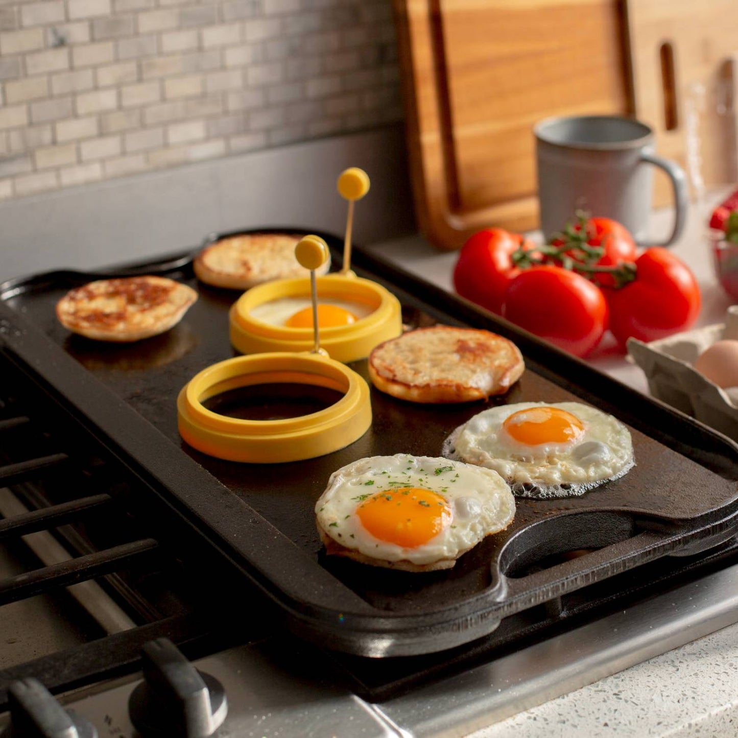 Cast iron griddle cooking eggs, English muffins, and egg rings on stovetop in kitchenware collection