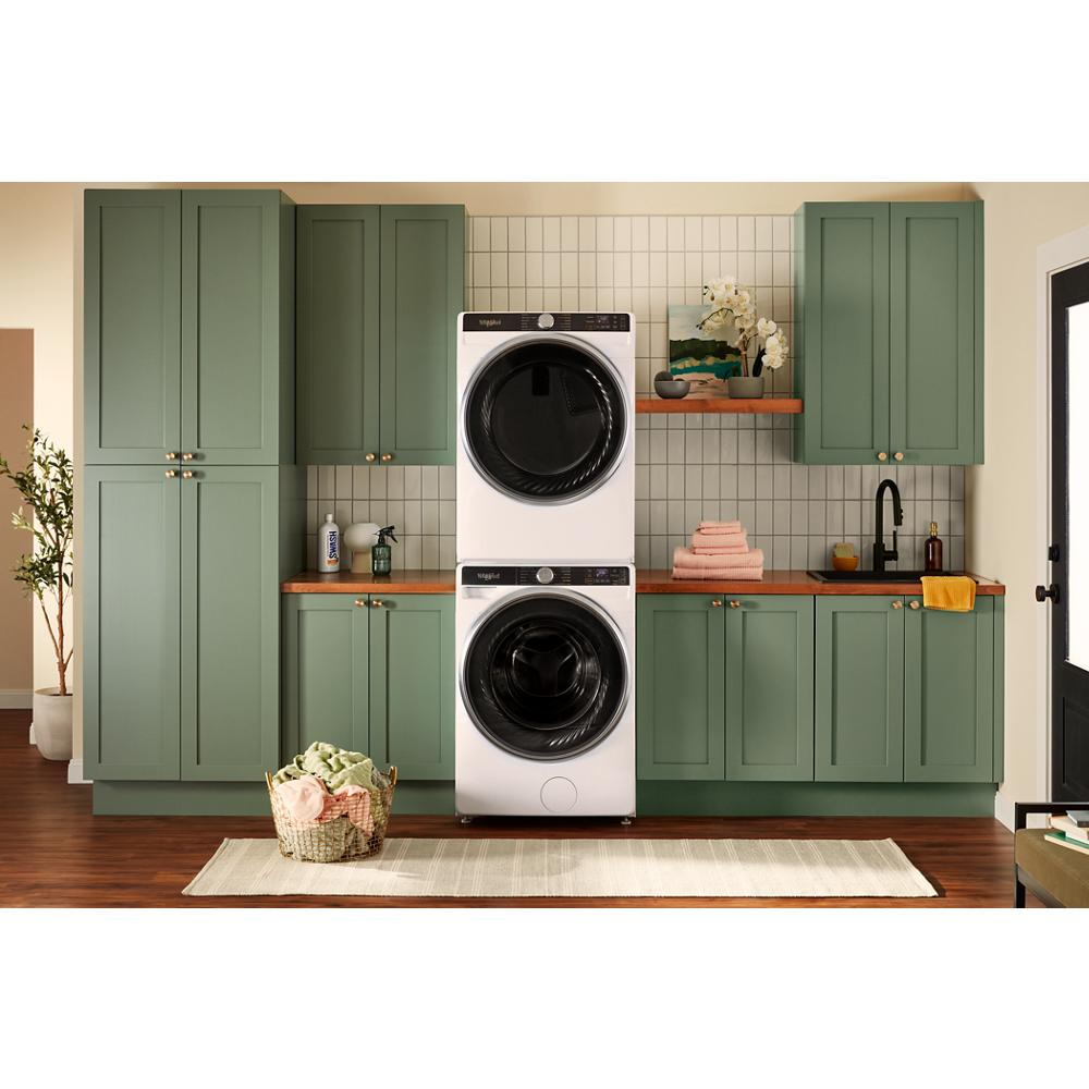 Stacked white smart front load washer and electric dryer in green kitchen cabinetry with wooden countertops and home decor