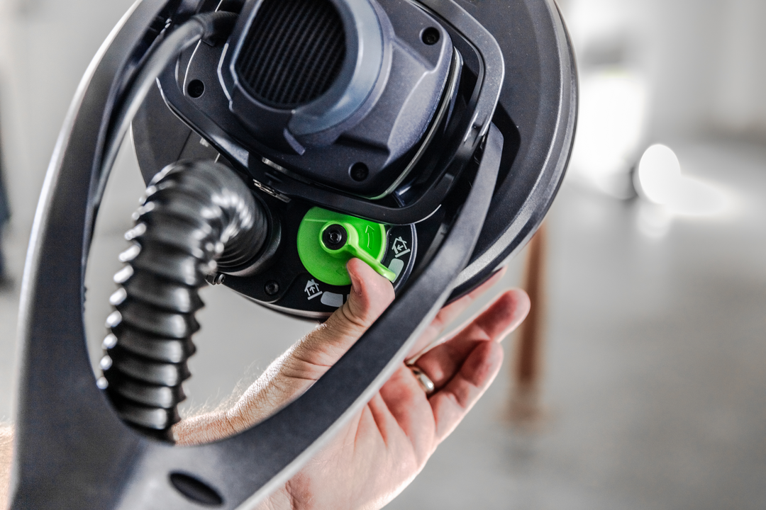 Hand adjusting green dial on Festool drywall sander with dust extraction in power tools for home improvement