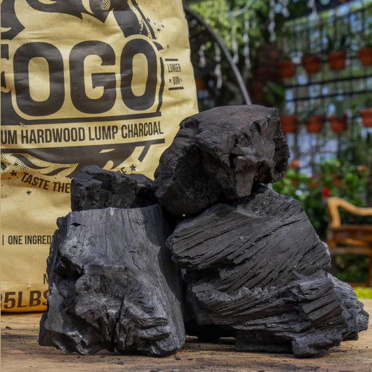 Large chunks of premium hardwood lump charcoal arranged in front of a branded bag outdoors in a garden setting
